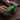Thumbnail for A person's hands holding a translucent green retro game controller over a dark wood table, with a black game controller and two small black accessories nearby.
