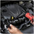 A person using a red cordless torque wrench to tighten a lug nut on a car engine, shown in a real-world garage or workshop environment.