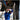 Thumbnail for A mechanic in a blue uniform works underneath a raised car using a red power tool in an auto repair shop.