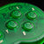 Close-up of a translucent green game controller showing the face buttons labeled X, A, Y, and B, with a start button and part of a brand logo on a dark background.
