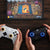 Two hands holding gaming controllers in front of a tablet displaying a board game.
